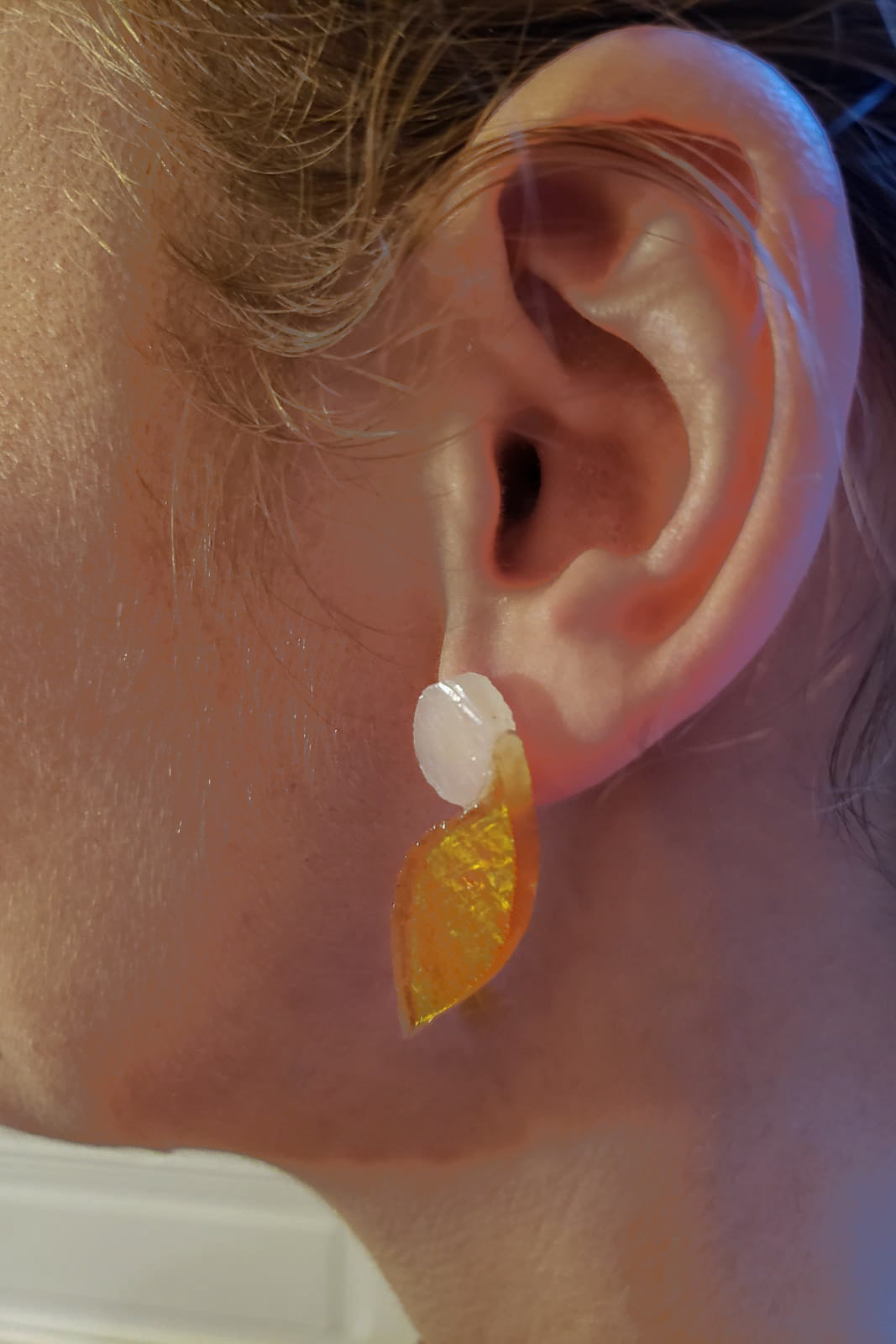 Ces boucles d’oreilles présentent une forme d’aile dans un verre jaune d’or aux reflets irisés, très changeant en fonction de la lumière. Elles sont surmontées d’un disque blanc laiteux. Elles sont agrémentées d’une attache à poussette de laiton doré.