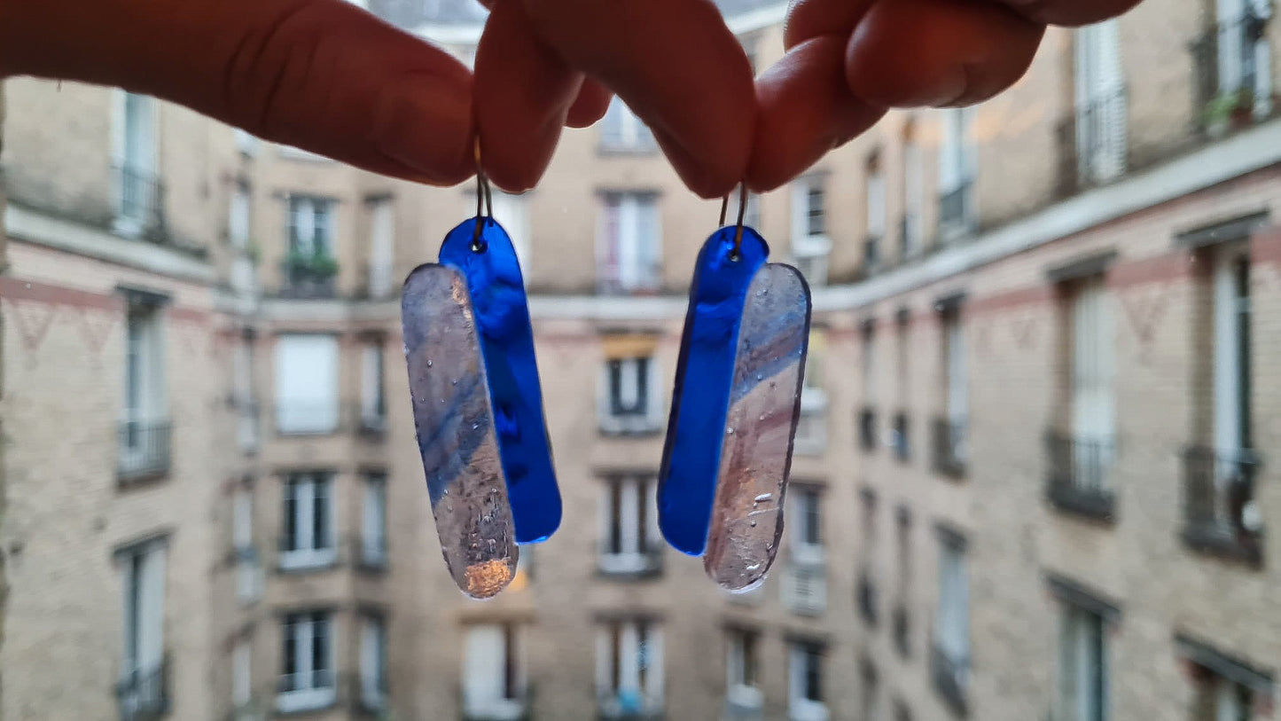 Ces boucles d’oreilles présentent deux verres de forme oblongue. L’un est bleu cobalt et l’autre présente un mélange de volutes rosées et bleutées sur fond clair. Le verre présente des bulles qui concourent à son charme :) Elles sont agrémentées d’attaches crochet en acier chirurgical. 