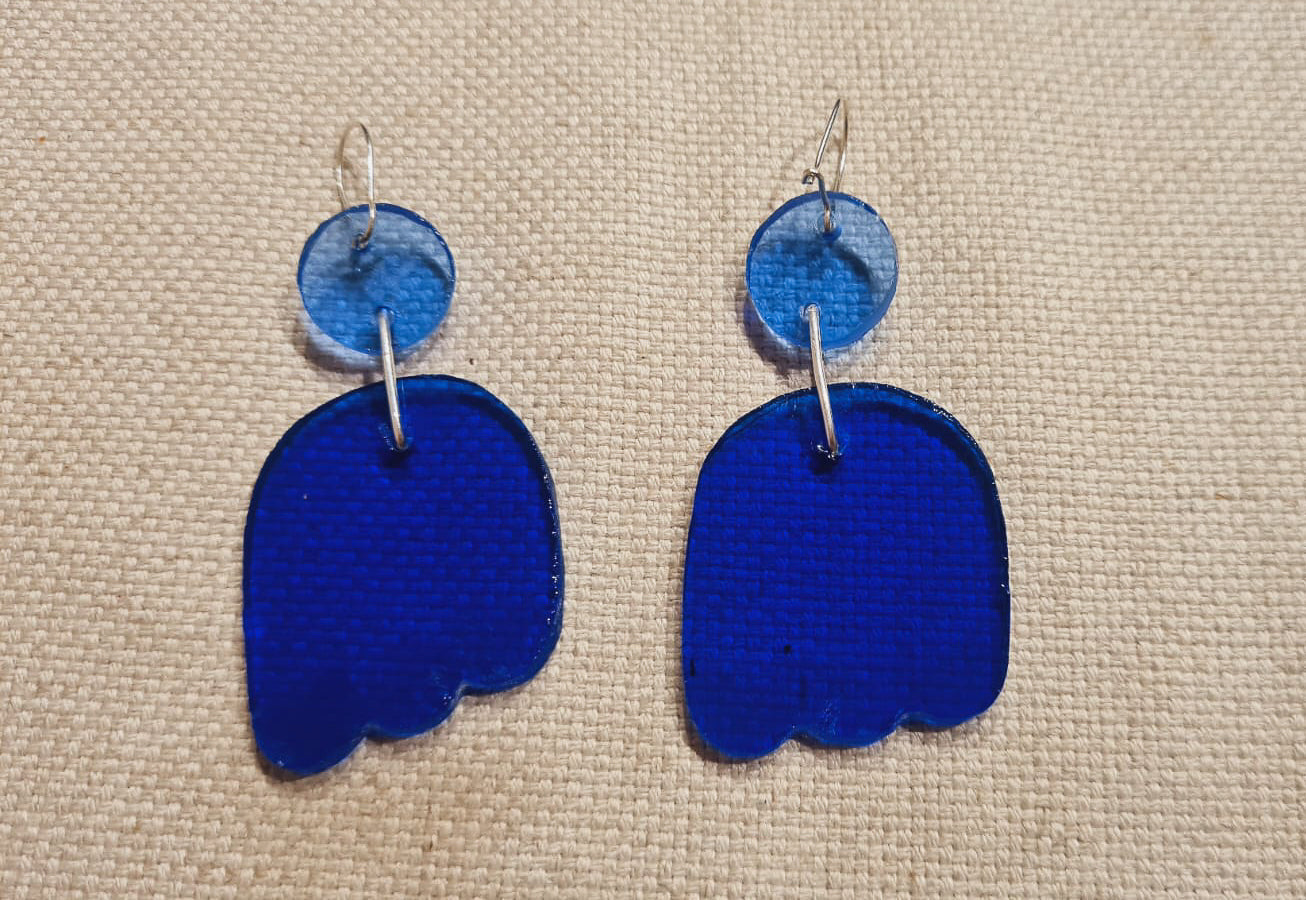 Ces boucles d’oreilles présentent un disque bleu clair qui surmonte une forme toute en courbes. Des gravures griffées ont été ajoutées dans le verre bleu cobalt. Elles sont agrémentées d’attaches crochet en laiton argenté. 