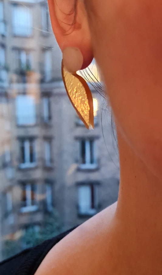 Ces boucles d’oreilles présentent une forme d’aile dans un verre jaune d’or aux reflets irisés, très changeant en fonction de la lumière. Elles sont surmontées d’un disque blanc laiteux. Elles sont agrémentées d’une attache à poussette de laiton doré. 